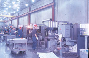 Line up of Dix Metals Nichols big twin mills (duplex mills) used for opposed face milling. The mills were built in the 1970s and ‘80s for the automotive industry, but Dix had them torn down to the bare castings and rebuilt into highly precise machining centers with sophisticated Mitsubishi CNC Controls. Tolerance on these machines is ±.001”. Shown observing the process is vp operations Pablo Garza (holding papers), who designed the 110,000 sq ft facility for Dix Metals.