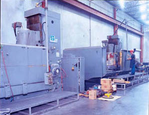 Two of Dix Metals’ large Schaffer rotary surface grinders. In the foreground is a 66” 200 hp unit. In the background is an 84” 200 hp unit. The company uses these to grind blanks to high levels of precision. A Jorgensen conveyor system (behind the grinders) is used to remove fine particles from machining fluids used on the disk grinders. 